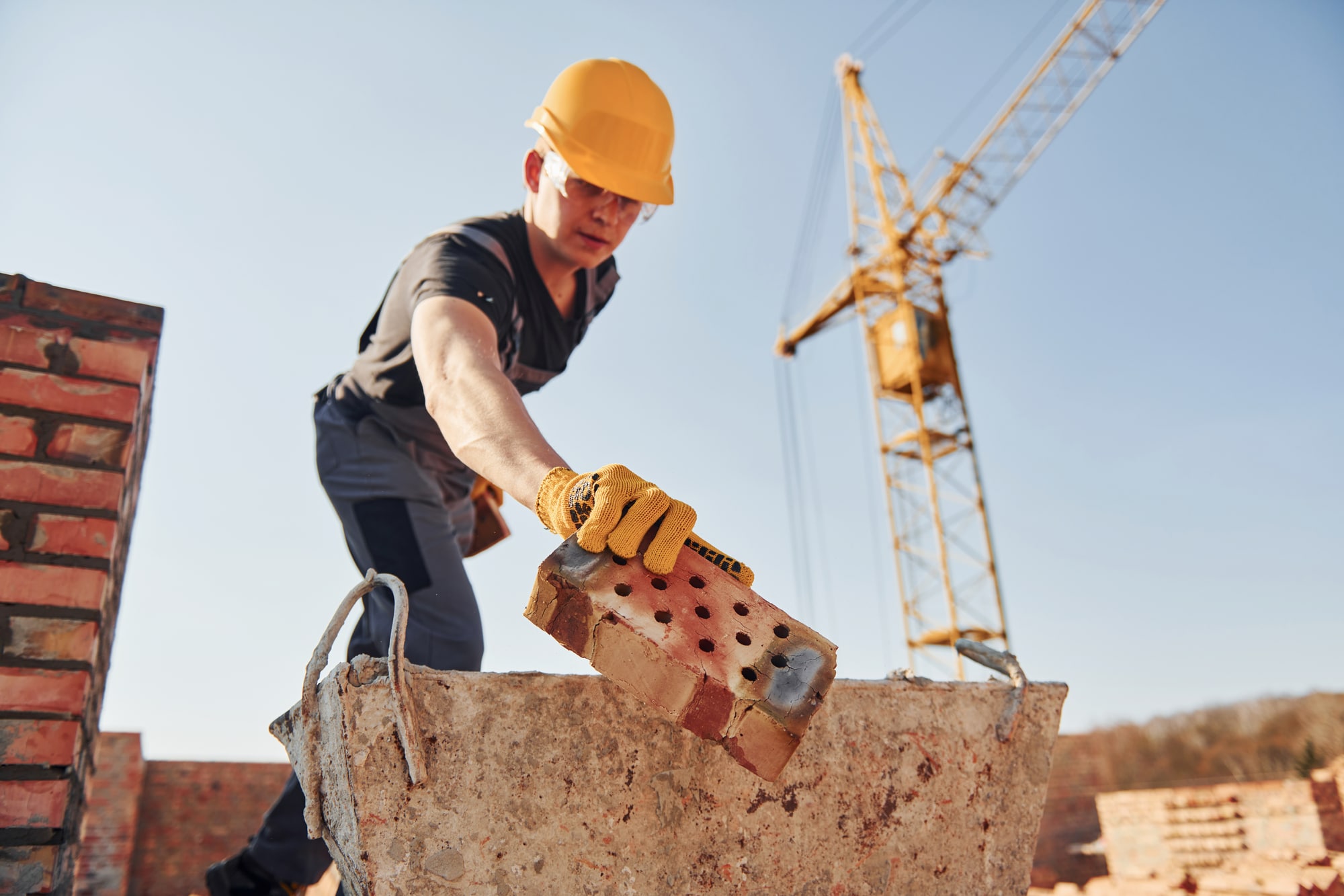 Holding brick and using hammer. Construction worker in uniform and safety equipment have job on building